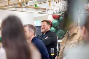 People socializing at an event with hanging glasses and green decorations visible in the background.