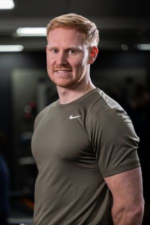 Athletic person wearing olive green Nike t-shirt poses in gym environment.