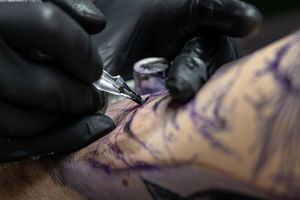 Black tattoo ink machine working on skin in close-up detail.