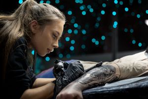 Tattoo artist working in a dark studio with blue bokeh lights in the background.