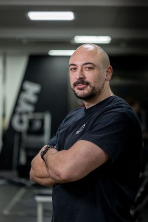 Fitness professional in black t-shirt stands confidently with arms crossed in gym setting.