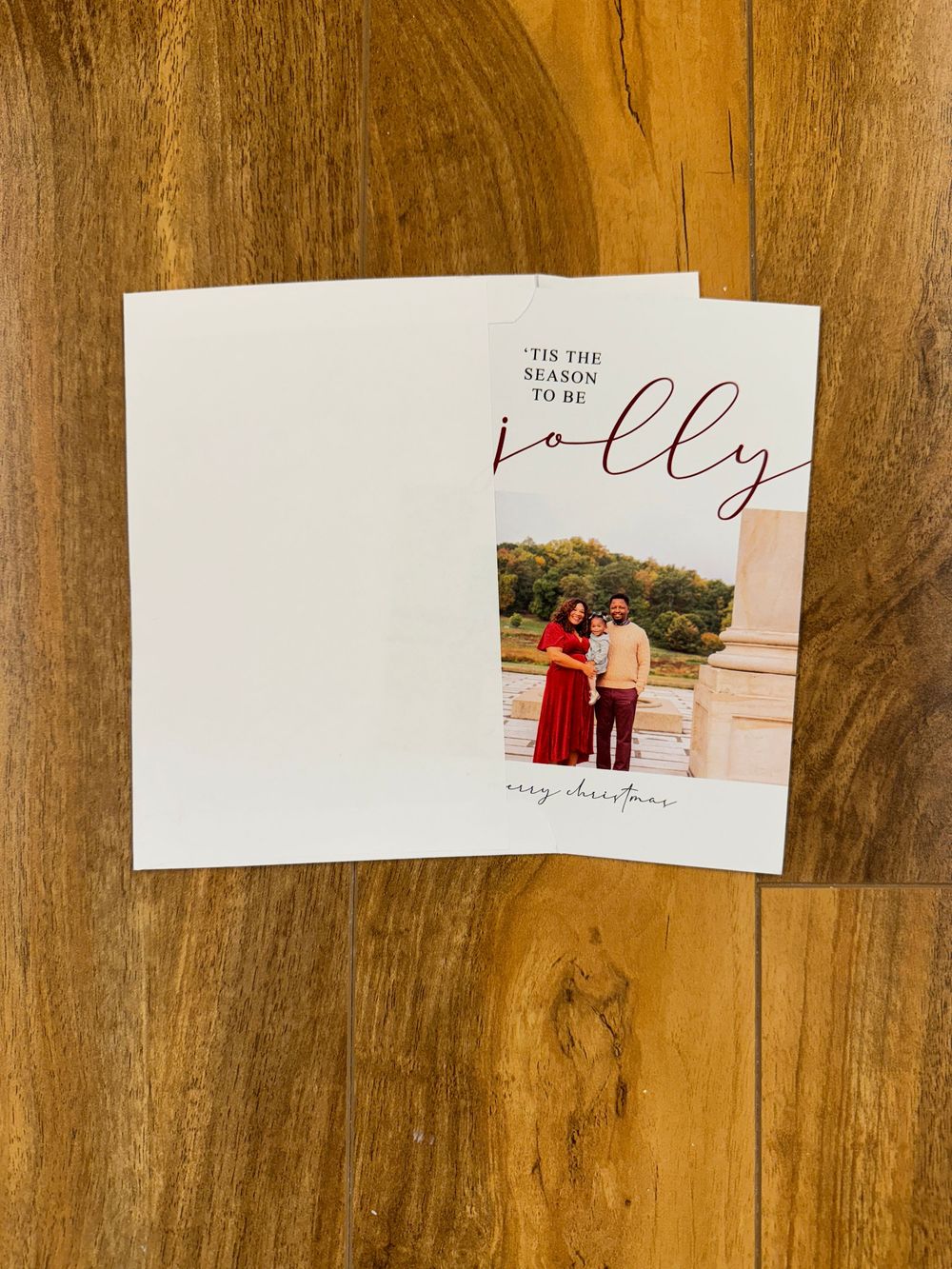 Holiday card: A white square greeting card with text 'jolly' and a small photograph lies on a wooden surface.