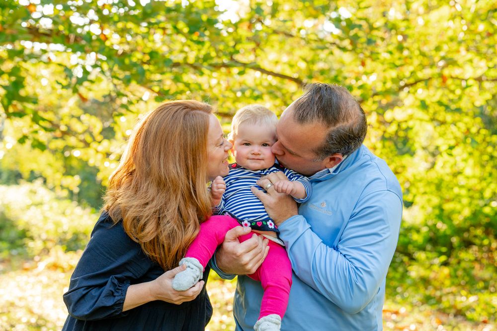 A family shares a tender moment outdoors on a sunny autumn day with golden leaves in the background.