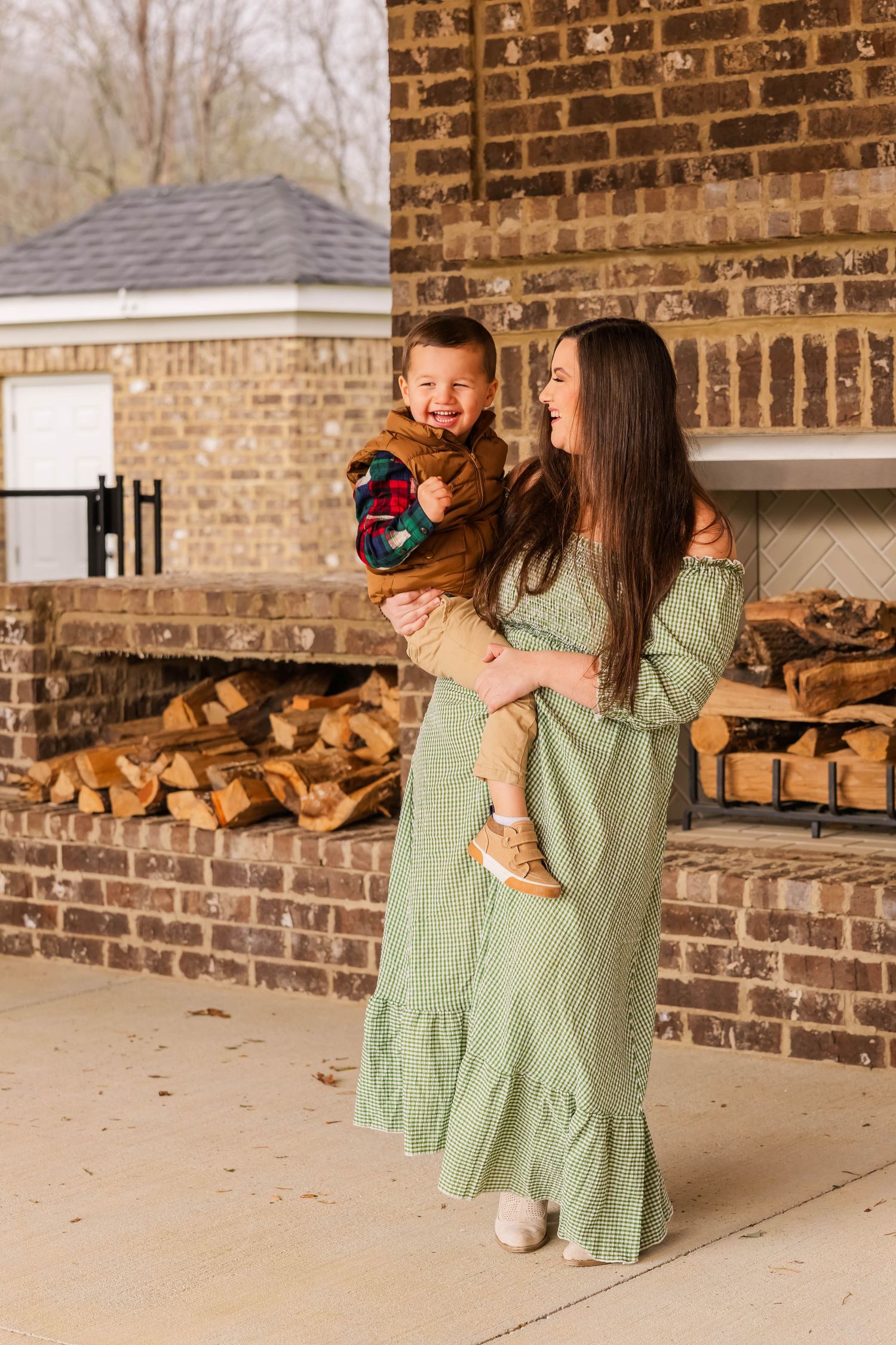 A tender moment captured by a brick wall with stacked firewood in the background.
