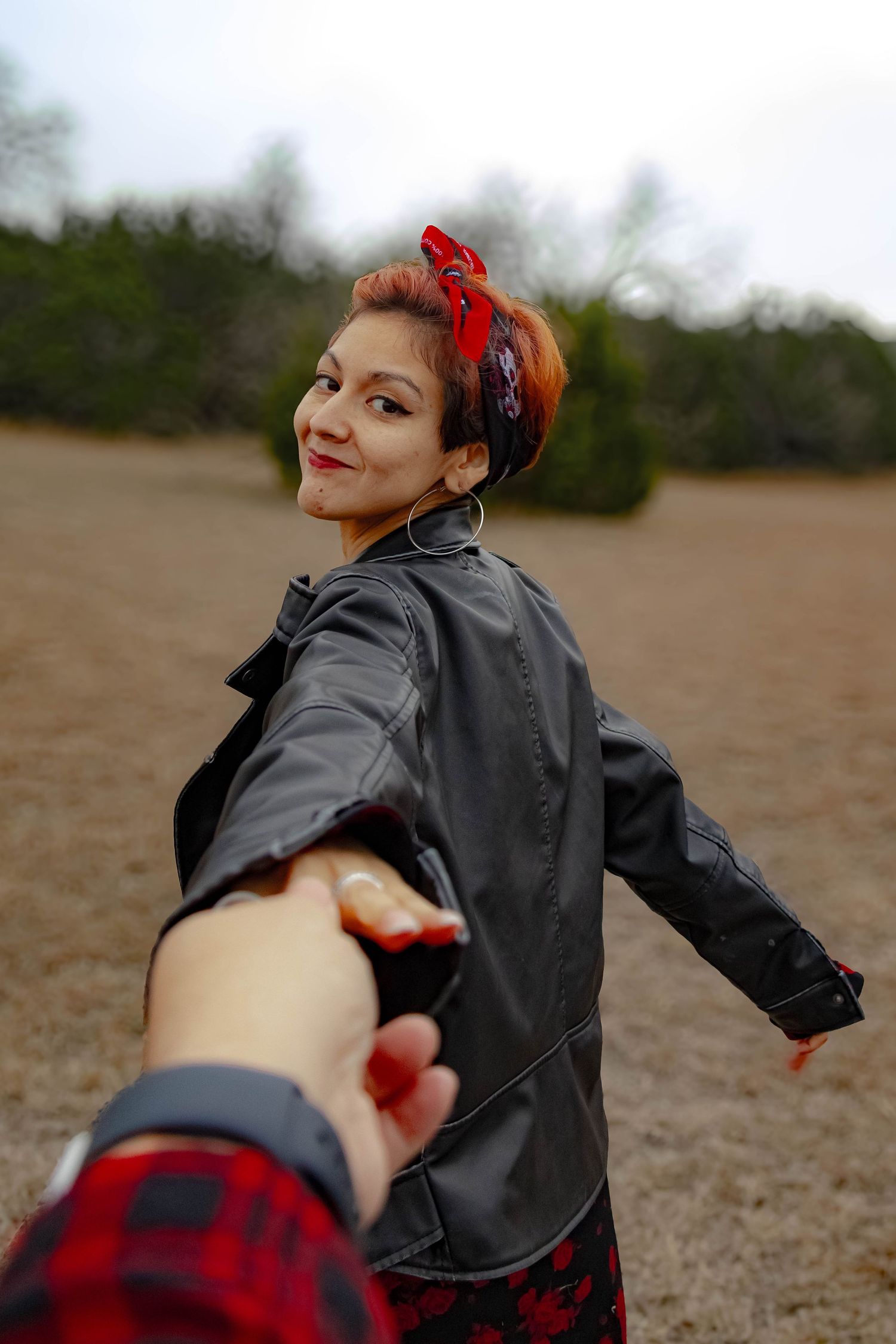 Person in black leather jacket and red bandana holds hand while walking through an outdoor field.