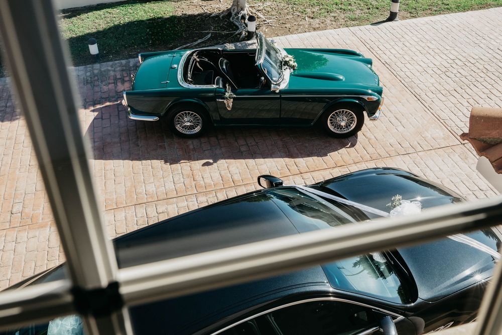 Vintage teal convertible sports car with chrome trim parked on brick driveway, viewed from above through a window.