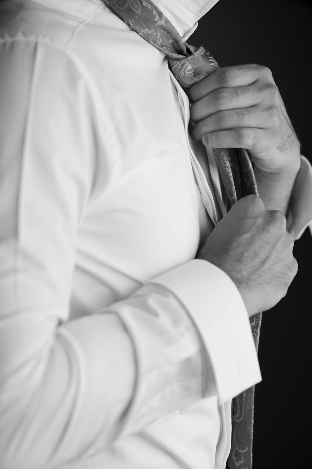 Close-up black and white shot of hands adjusting a necktie while wearing a crisp white dress shirt.