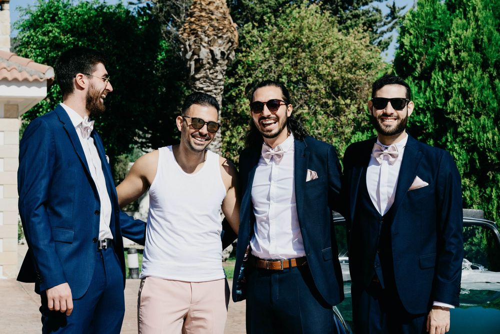 Groomsmen in navy suits and sunglasses laugh together outdoors during a wedding photo session.