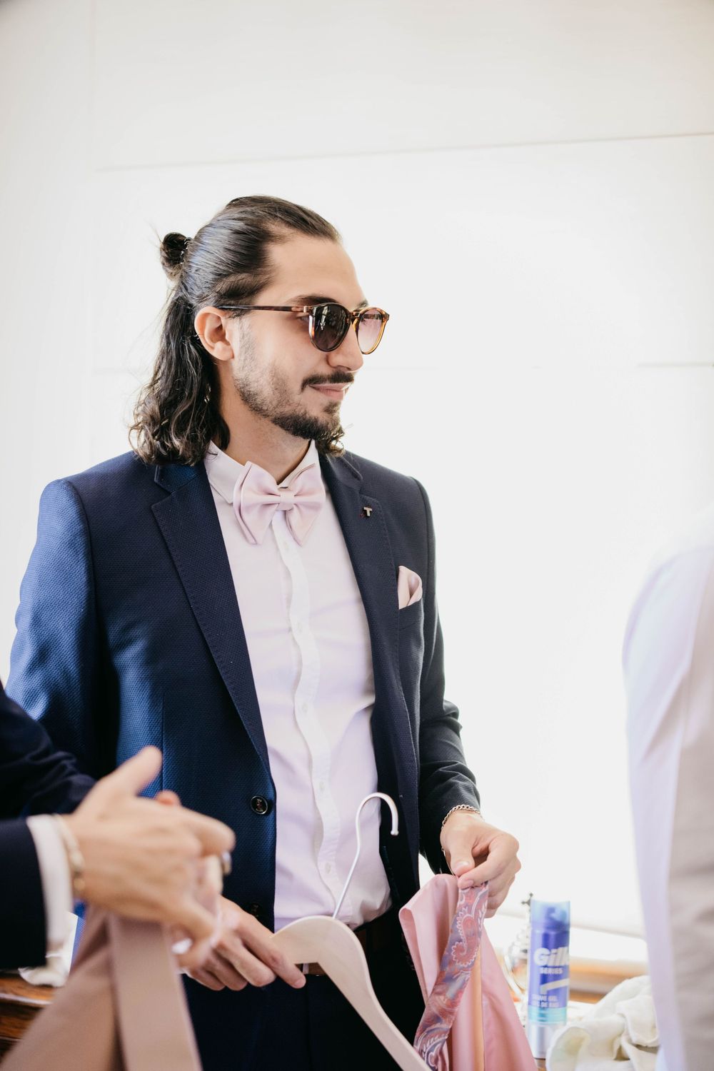 A person in a navy suit and light pink shirt wearing glasses and with hair in a half-up style gestures during conversation.