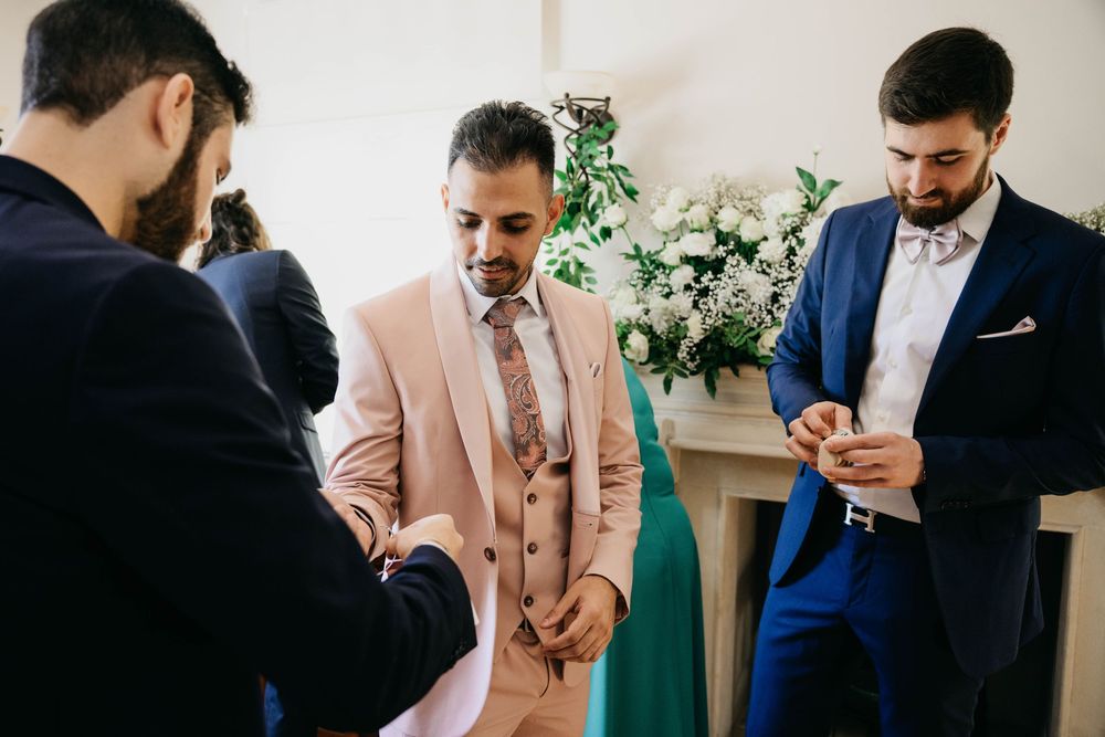 Three people dressed in suits, with one wearing pink and one in navy, gathered together at a formal event.