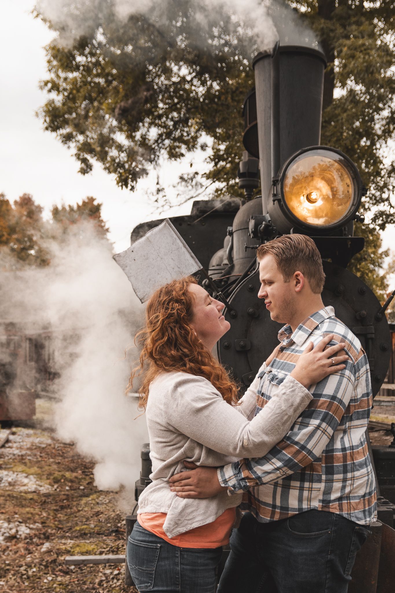 A romantic couple embraces in front of a vintage steam locomotive with atmospheric smoke.