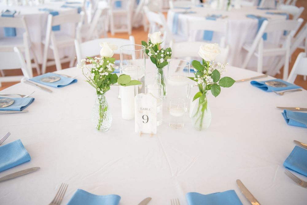 Wedding reception tables set with small glass vases of greenery and numbered table cards.