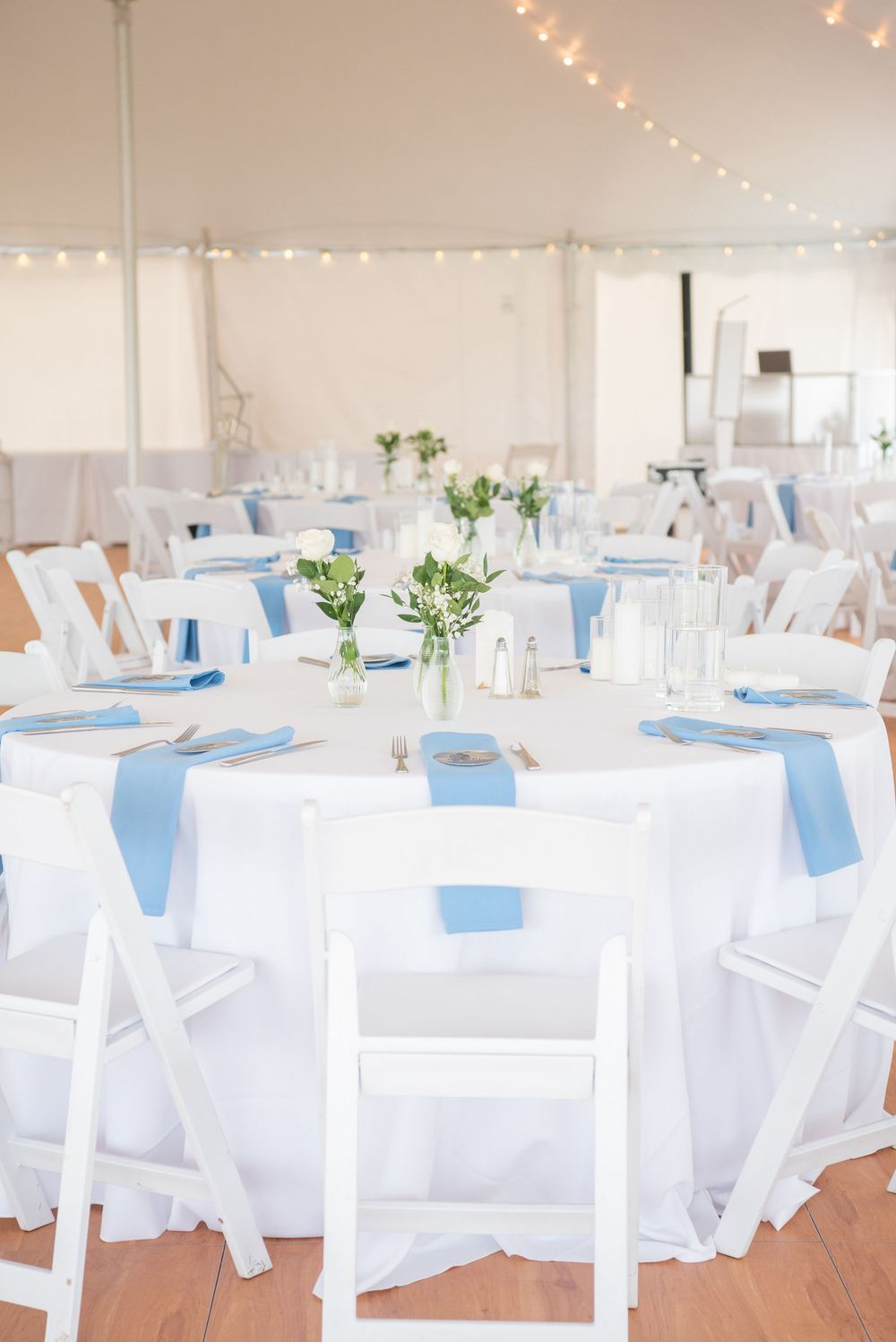 White wedding reception tent with blue accents and string lights creating an airy atmosphere.