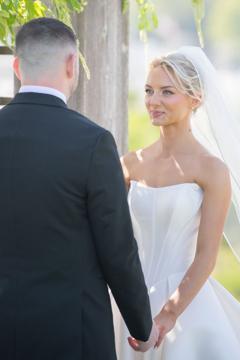 Wedding ceremony under a pergola with hanging greenery and natural sunlight.