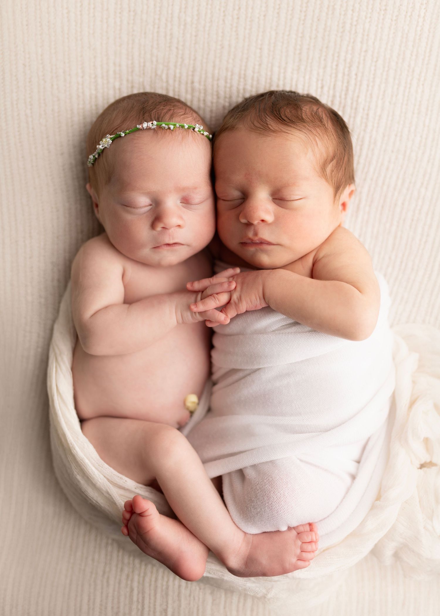 twins snuggle on a blanket and hold hands with interlocking fingers. Neutral fabric wraps them up. Newborn Photos for Janina's Photo session