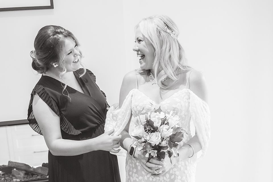 A heartwarming black and white wedding moment showing two people sharing laughter together, one holding a floral bouquet.