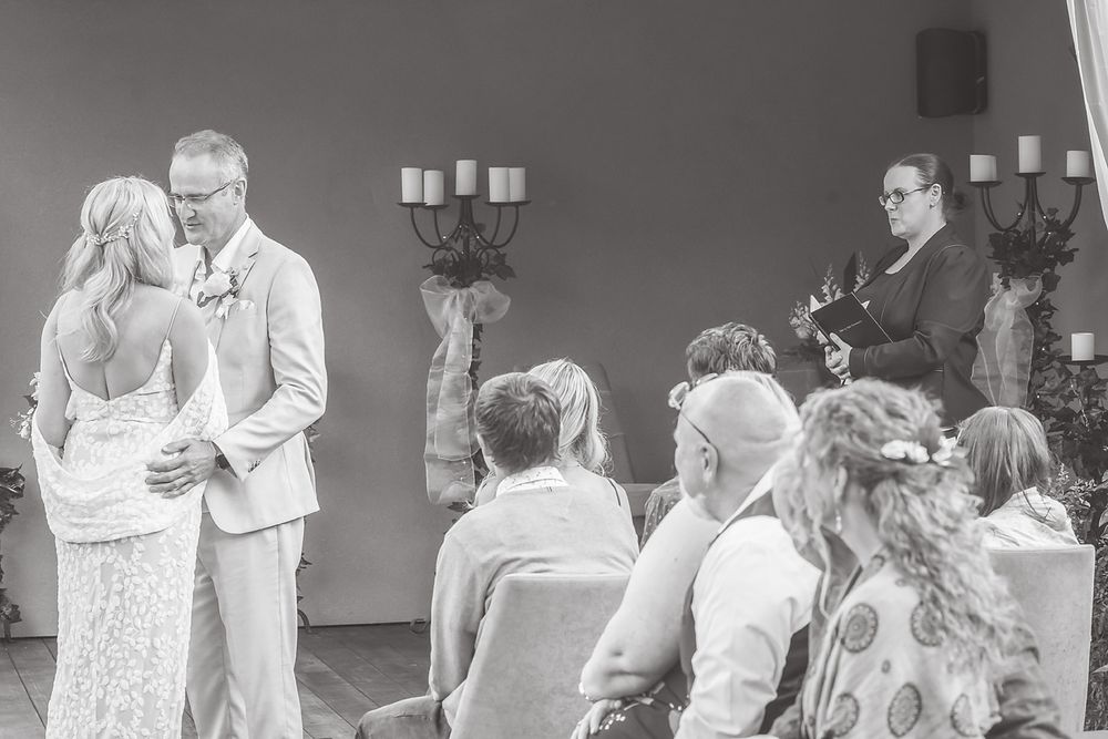 A couple shares their first dance at an intimate wedding reception while guests look on in black and white.