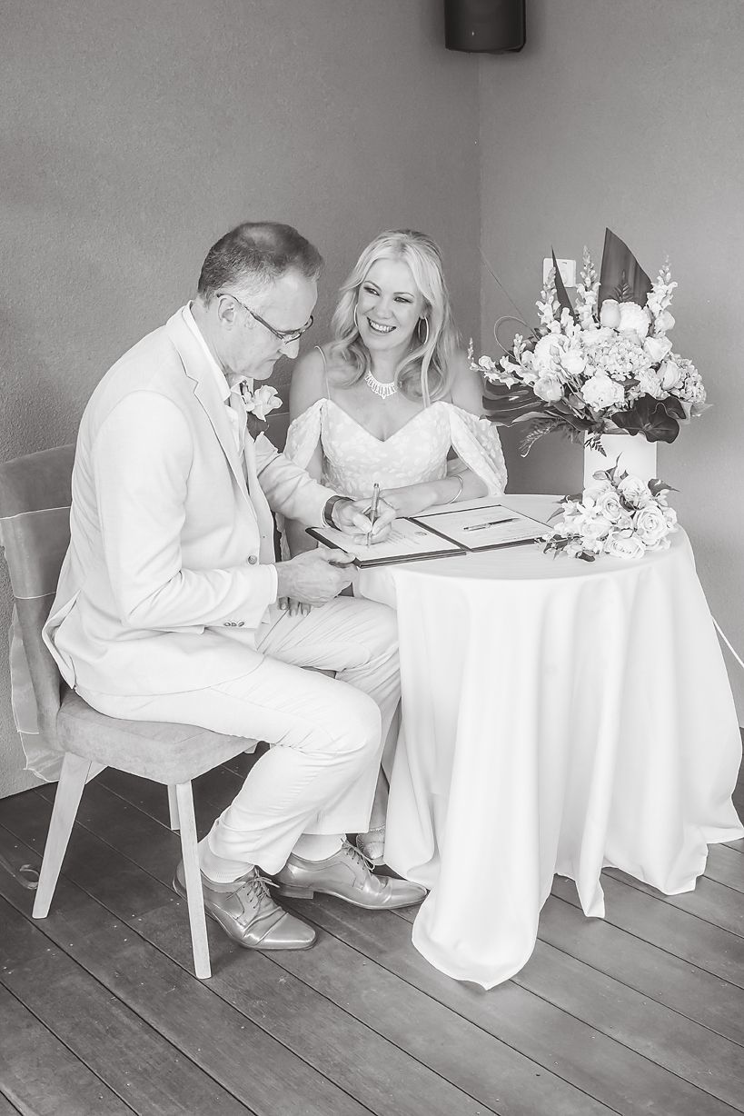 A series of black and white photos showing two individuals signing documents at a white table with flowers.