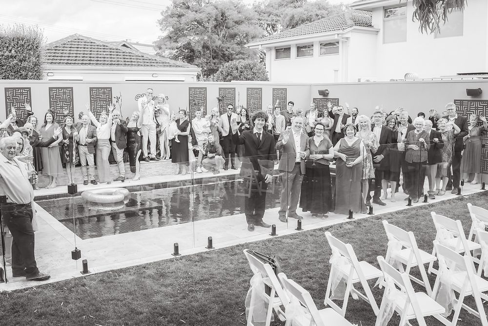 A crowd of wedding guests throwing white rose petals in celebration outside a venue.