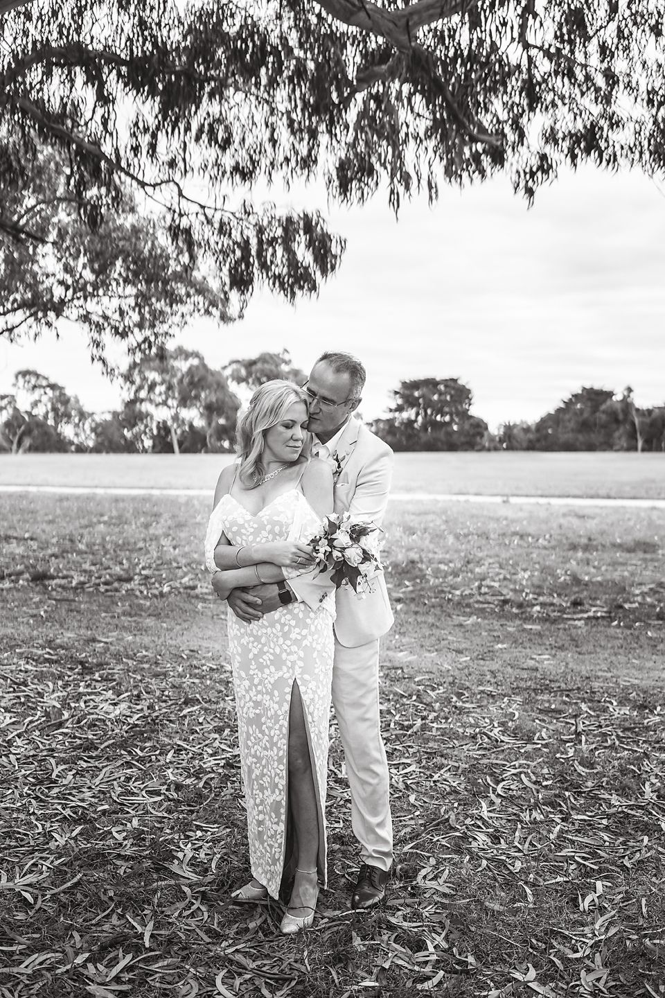 Black and white photo of couple embracing in a rustic outdoor setting among gum trees.
