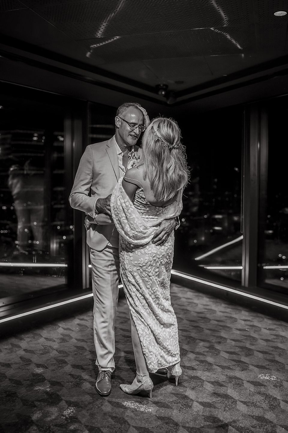 A couple in formal attire shares a romantic dance in a dimly lit venue with a patterned carpet floor.
