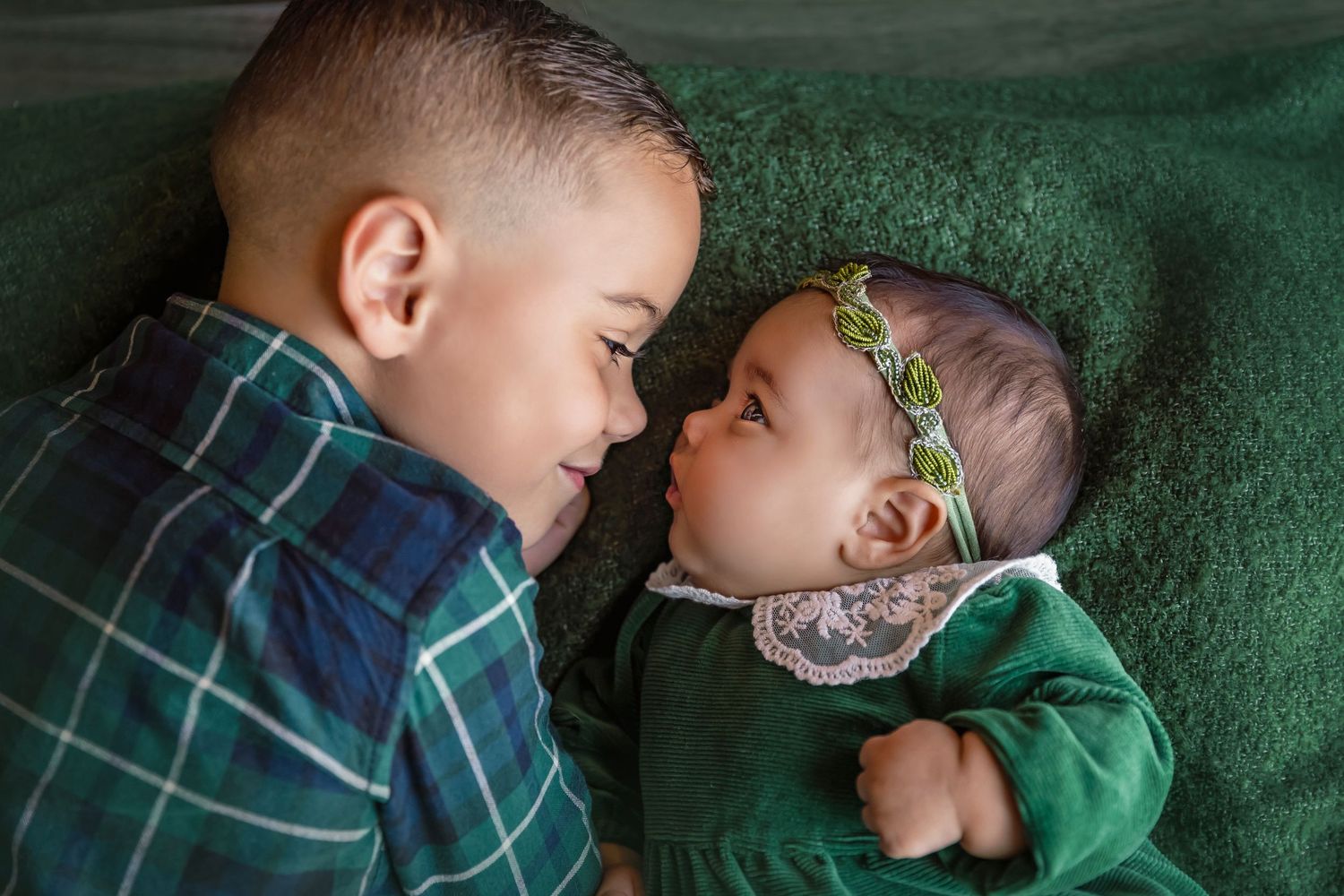 big brother and baby sister lay side by side looking at each other