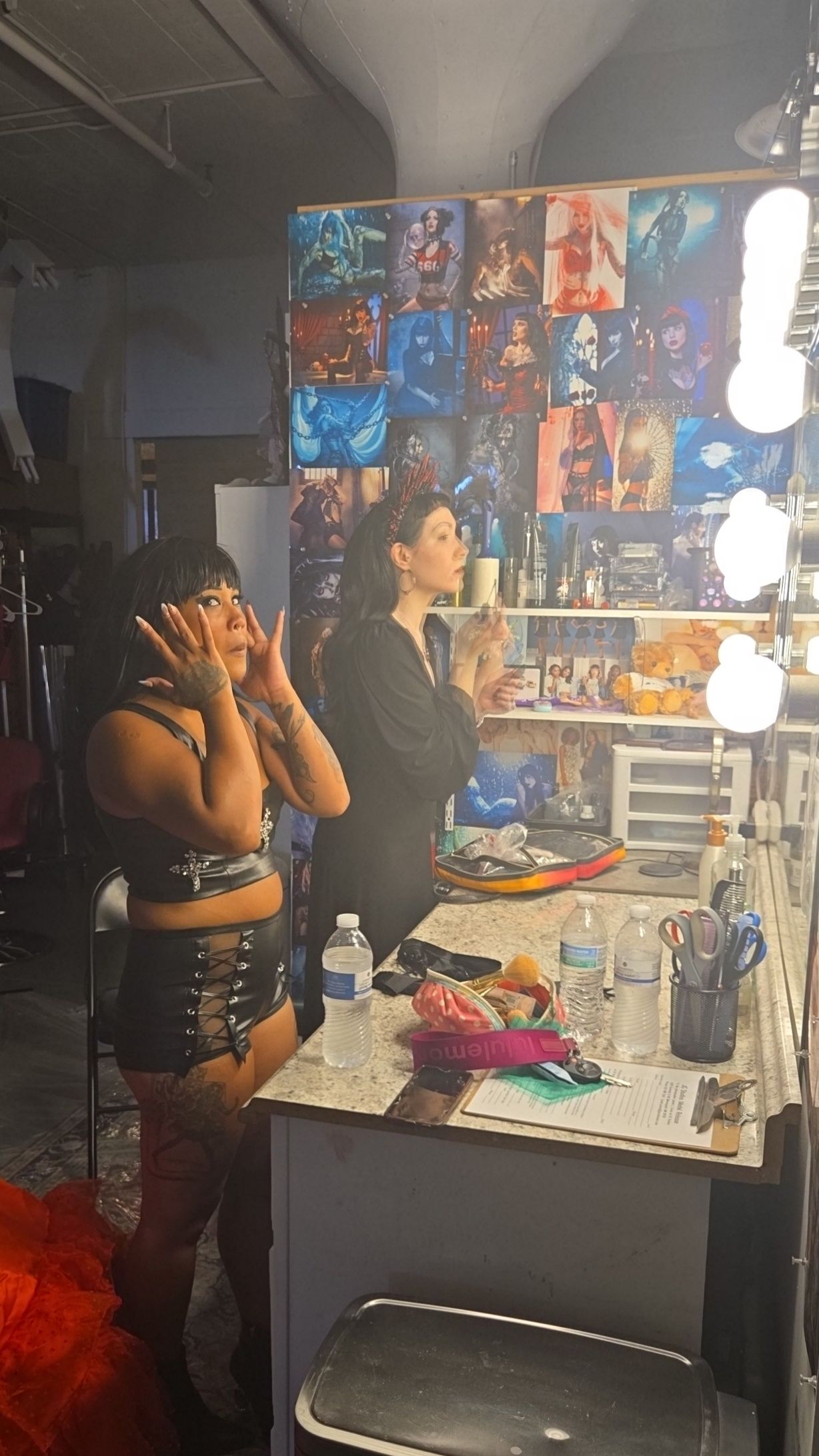 Behind the scenes view of a dressing room with makeup vanity mirrors, theatrical posters, and performers getting ready backstage.