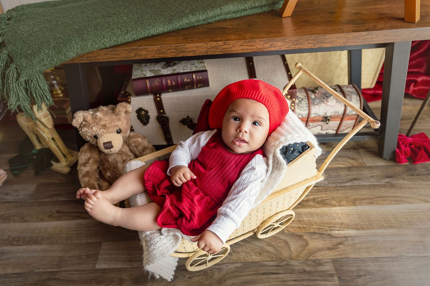 bebe de 4 meses esta sentada dentrp de un cochecito de metal color crema, esta esta vestida de rojo y blanco para sus imagenes