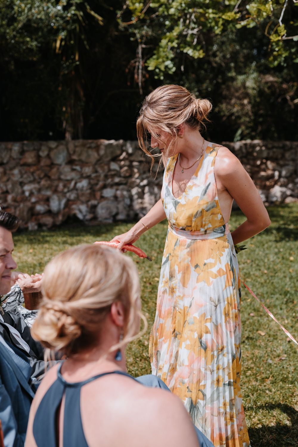 Trauzeugin, im gelben, geblümten Sommerkleid, hilft Hochzeitsgästen, an einem sonnigen Sommertag, während der Trauung mit den Eheringen.
