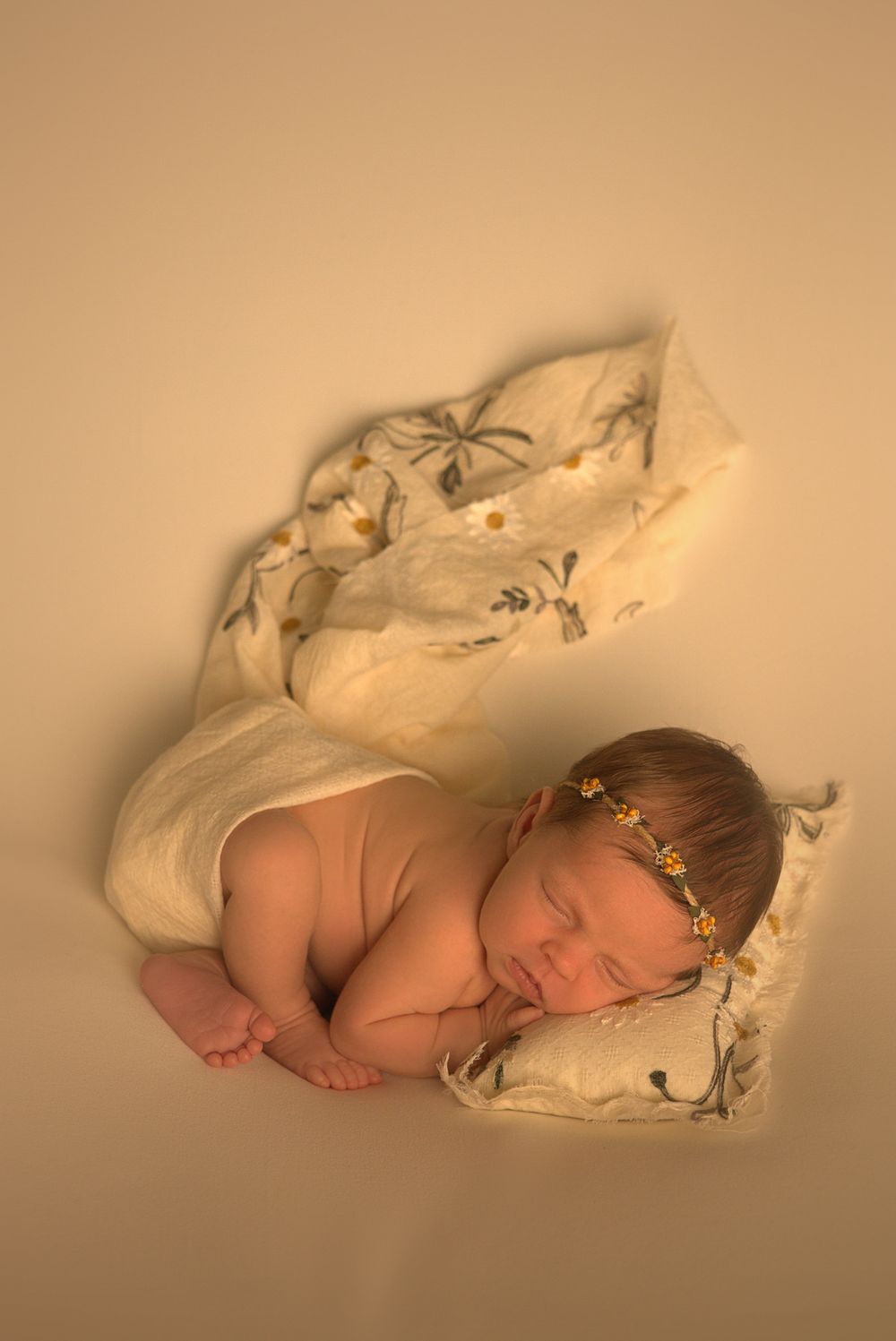 Sleeping newborn wrapped in soft white fabric with delicate crown accessory.