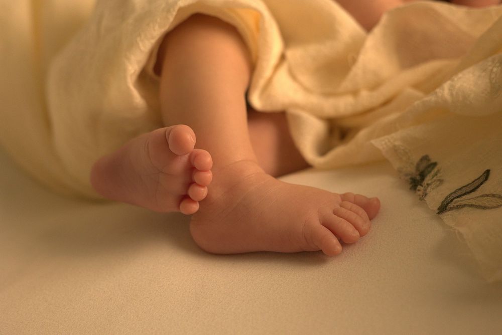 Close-up of tiny newborn baby toes wrapped in soft cream-colored fabric.