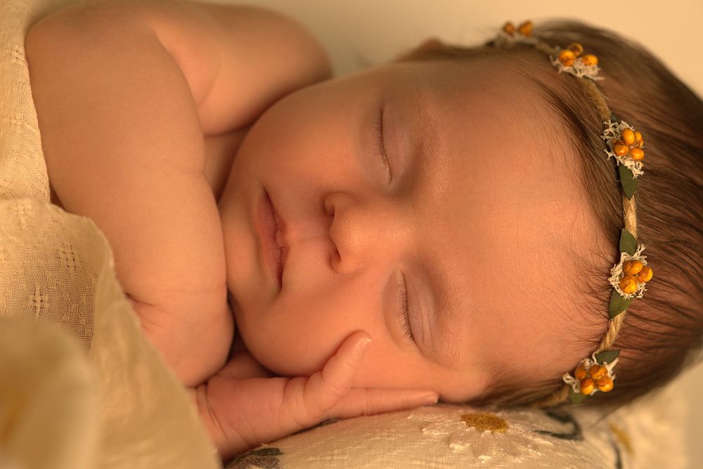 Peaceful newborn portrait with tiny crown against cream background.
