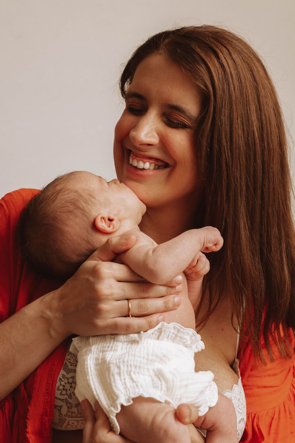 A joyful woman in red holds and smiles at a baby wearing a white diaper.