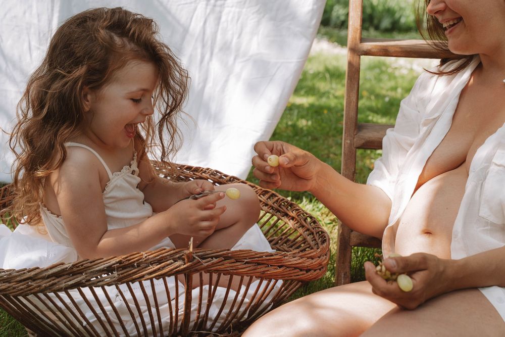A young child and adult sitting together in wicker furniture while sharing a light moment in natural sunlight.
