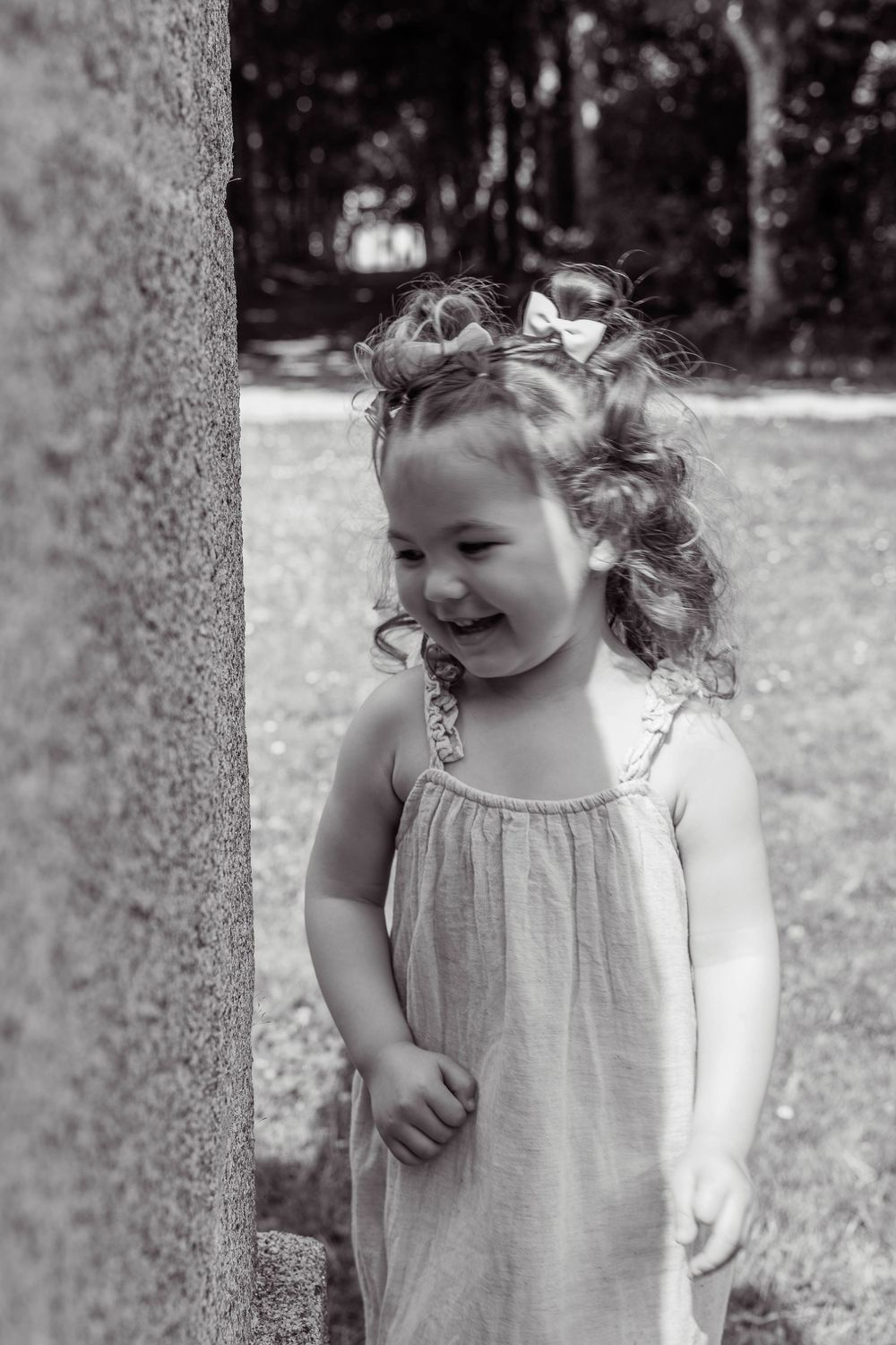 Black and white portrait of a young child with curly hair wearing a light summer dress, laughing joyfully outdoors.