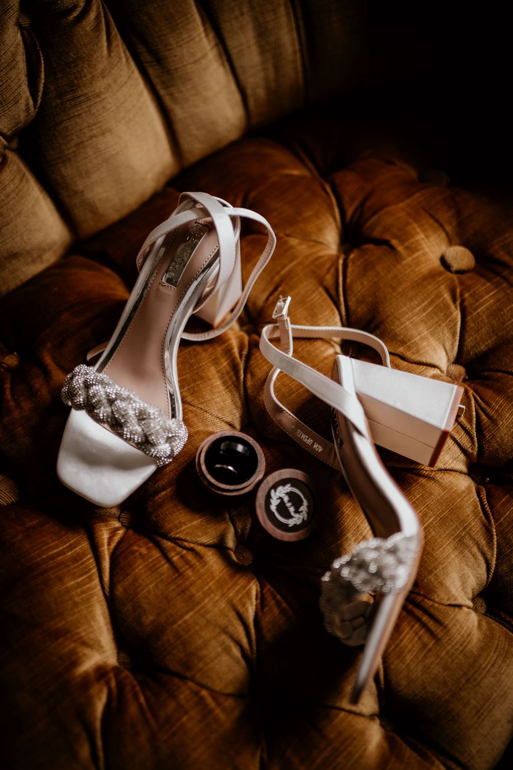 A series of wedding details showing white high heels and accessories arranged artistically on a tufted brown leather surface.