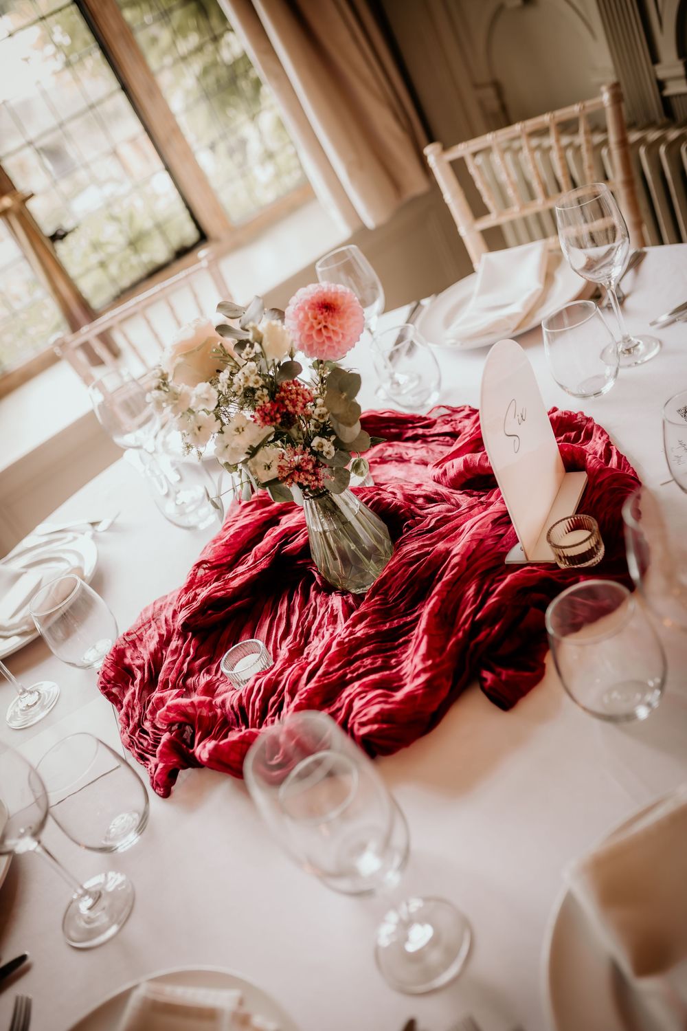 Wedding table setting with a luxurious red velvet runner, pink floral centerpiece, and elegant wine glasses.