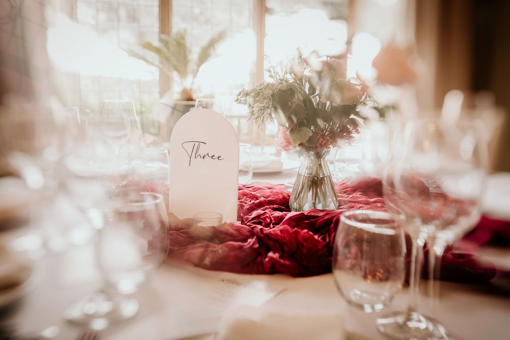 Elegant table settings with glowing candlelight and dark red floral arrangements create a romantic wedding reception atmosphere.