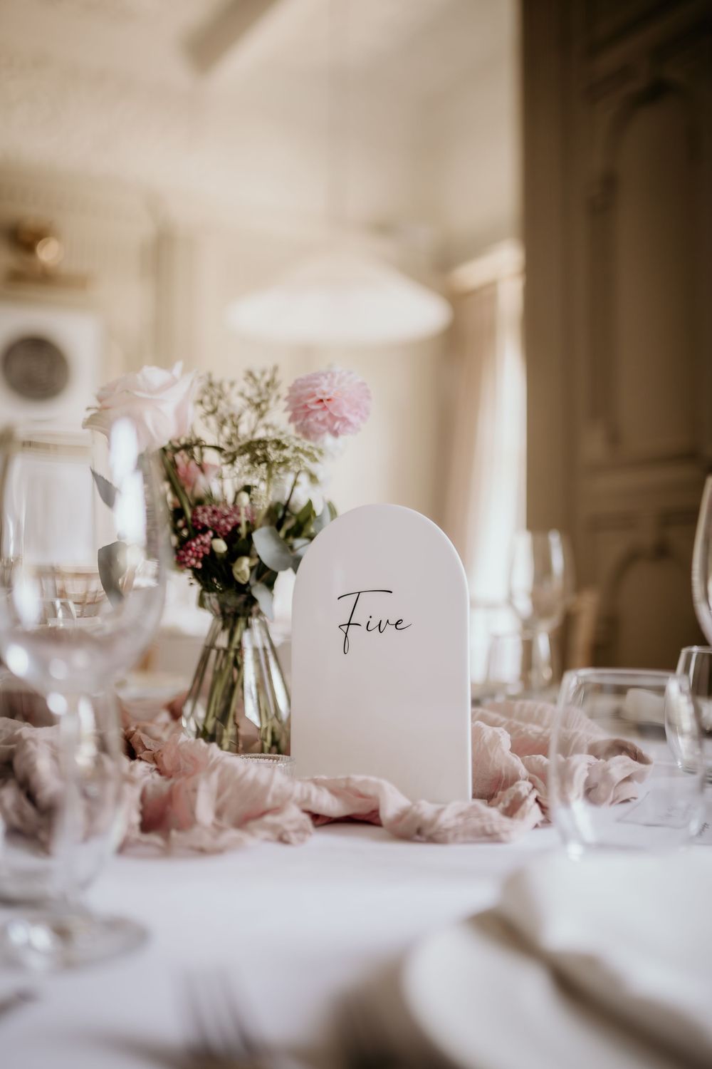 Elegant wedding reception table setting with white linens, delicate floral centerpieces and table number cards.