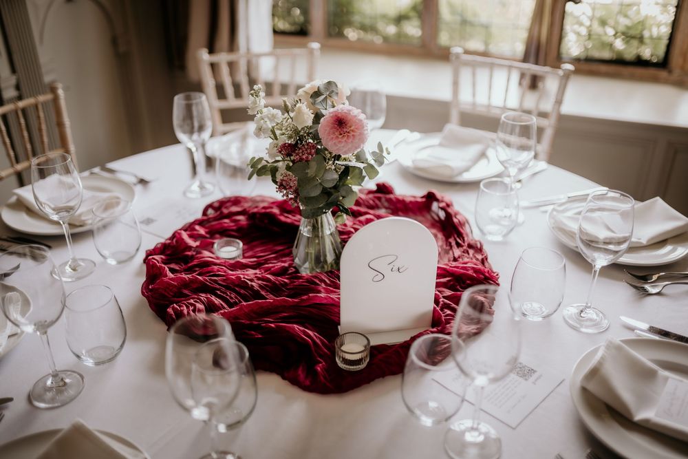 An elegant table setting with a deep red velvet centerpiece, pink floral arrangement, and crystal wine glasses for a formal event.