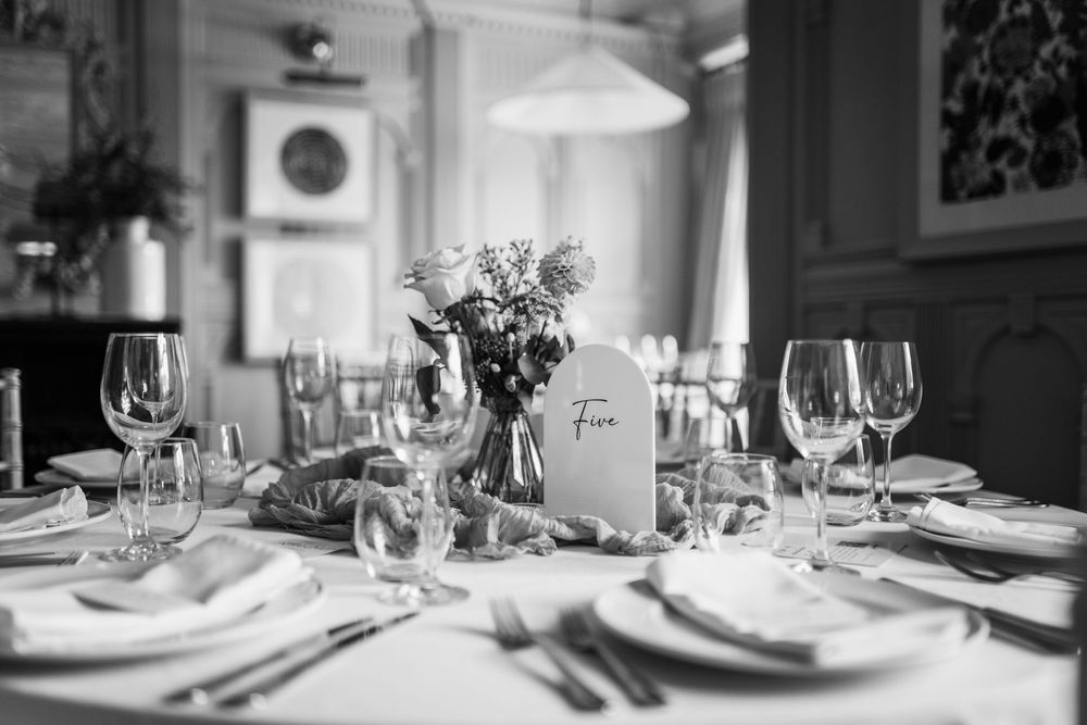 Professional table settings at a fine dining restaurant with elegant wine glasses and white tablecloths in monochrome.