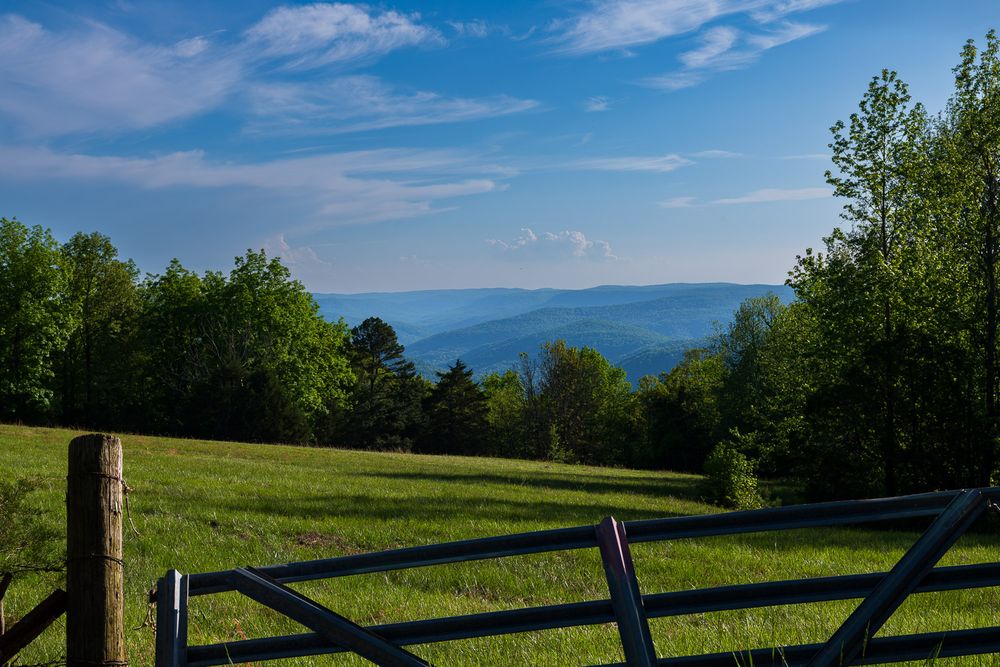 Scenic mountain view through a wooden farm gate with green fields and blue ridgelines in background. Compton Arkanas Buffalo National River