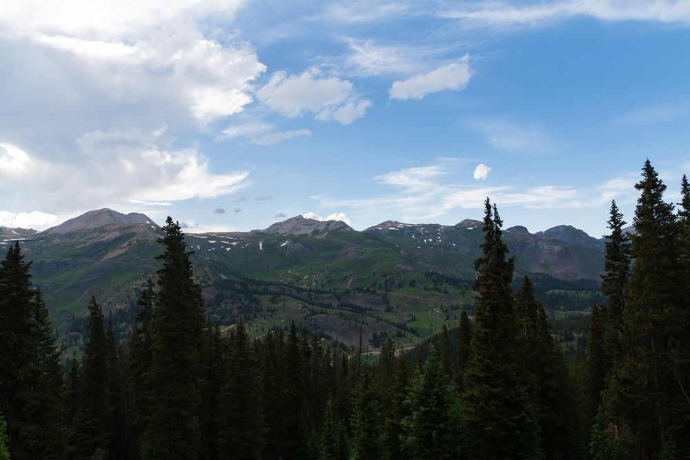 Mountain range with snow-capped peaks and pine forest under a partly cloudy sky. San Juan Mountains Colorado
