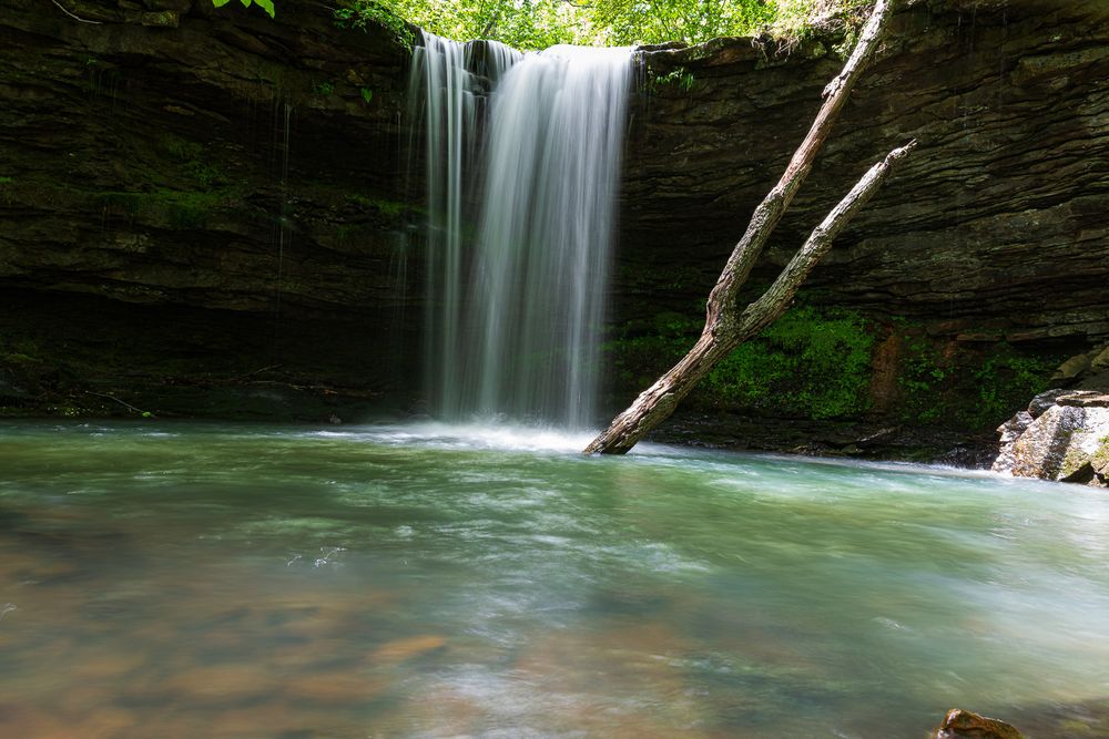 Serene Mule Trail waterfall cascading into a clear green pool surrounded by lush forest and rocky walls. Hawksbill Crag Trail