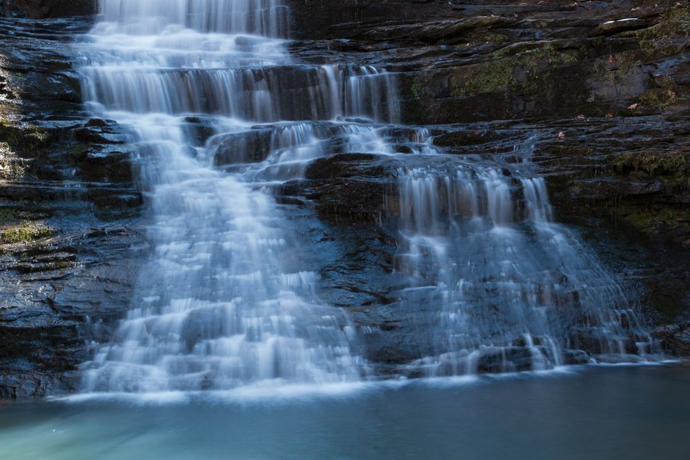 Silky cascading waterfall flowing over layered rock ledges into a tranquil blue pool below. Native American Falls Northwest Arkansas