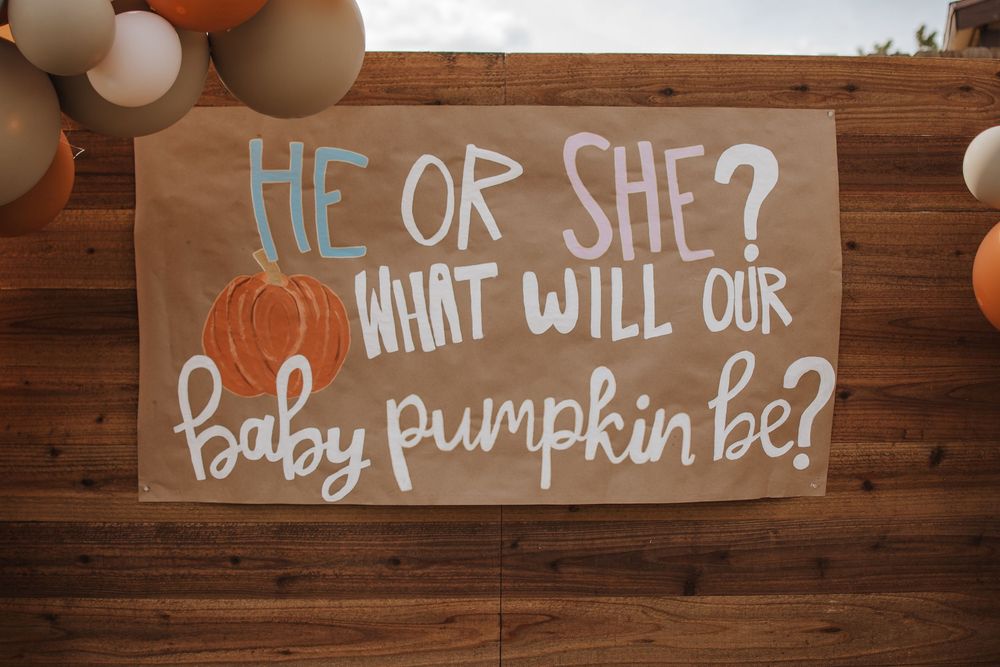 A rustic wooden sign for a gender reveal party with 'He or She? What will our baby pumpkin be?' in white and blue text.