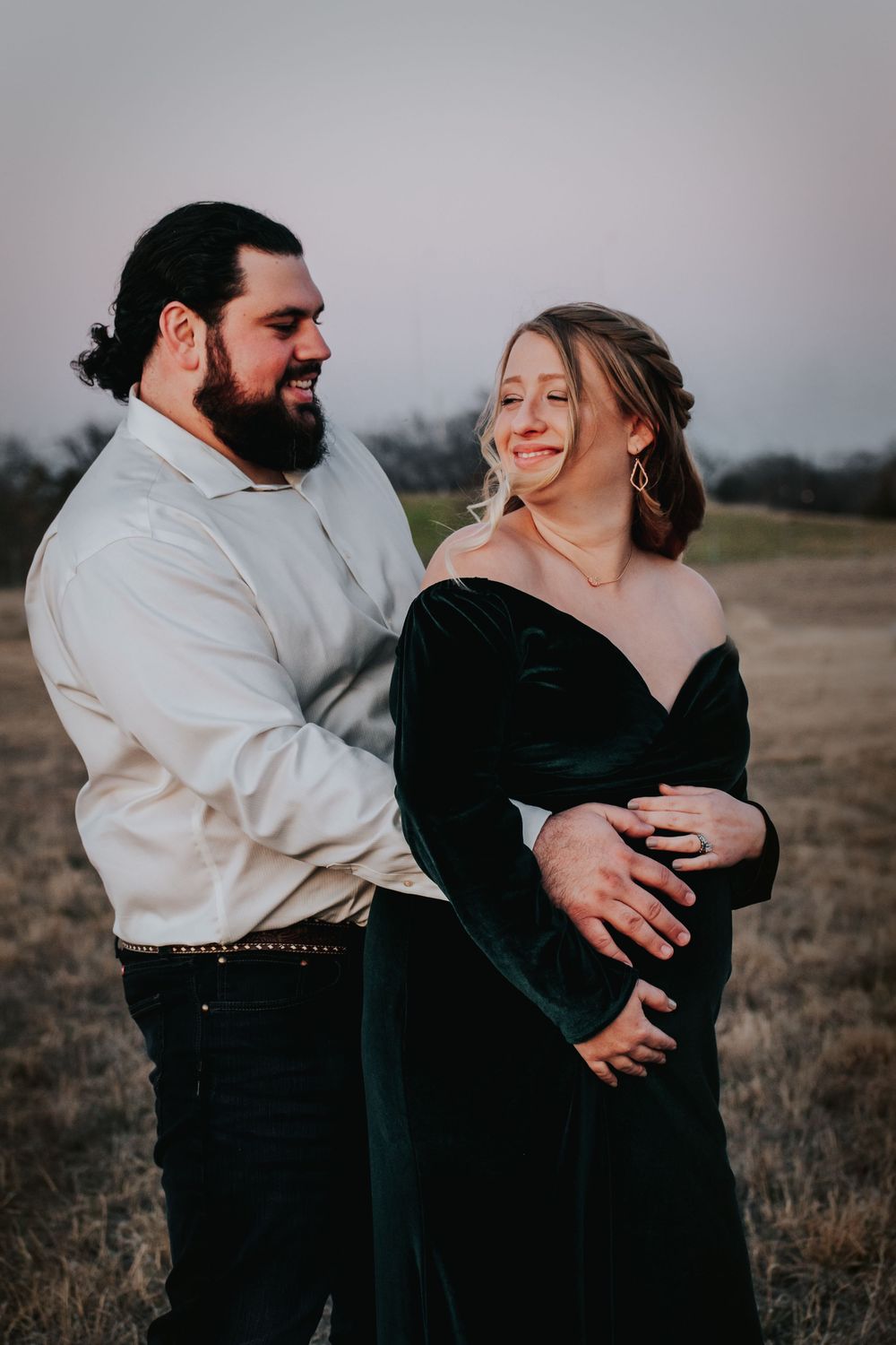 A couple shares an intimate moment outdoors at dusk, with her wearing an elegant black velvet dress.