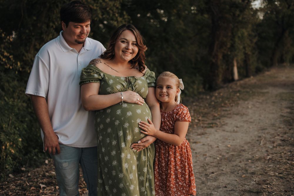 A family in coordinating earth-tone outfits walks together on a wooded trail in soft lighting.