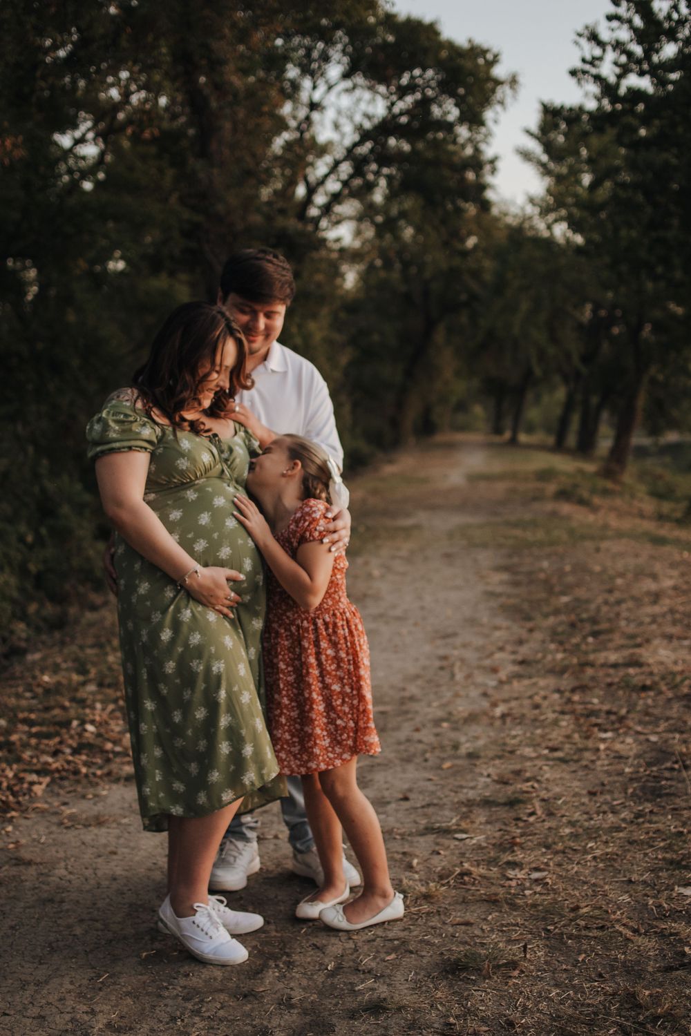 A family shares a tender moment embracing on a tree-lined dirt path during golden hour.