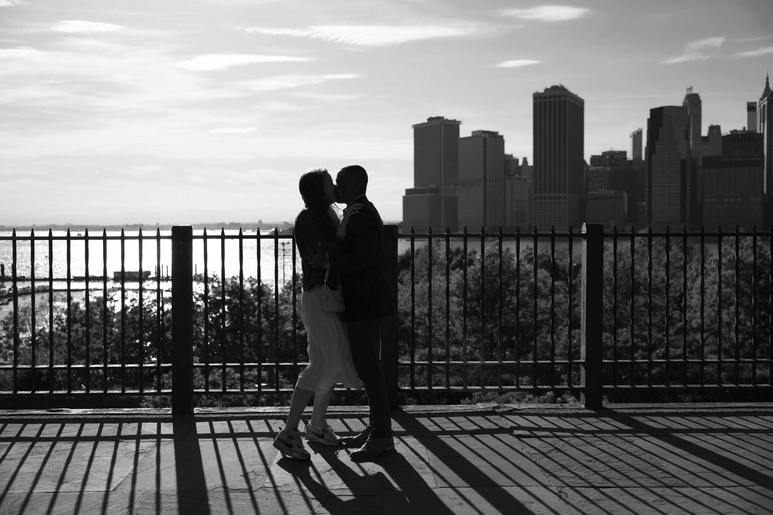 Romantic couple silhouetted against NYC skyline sharing a kiss on a rooftop terrace in black and white.